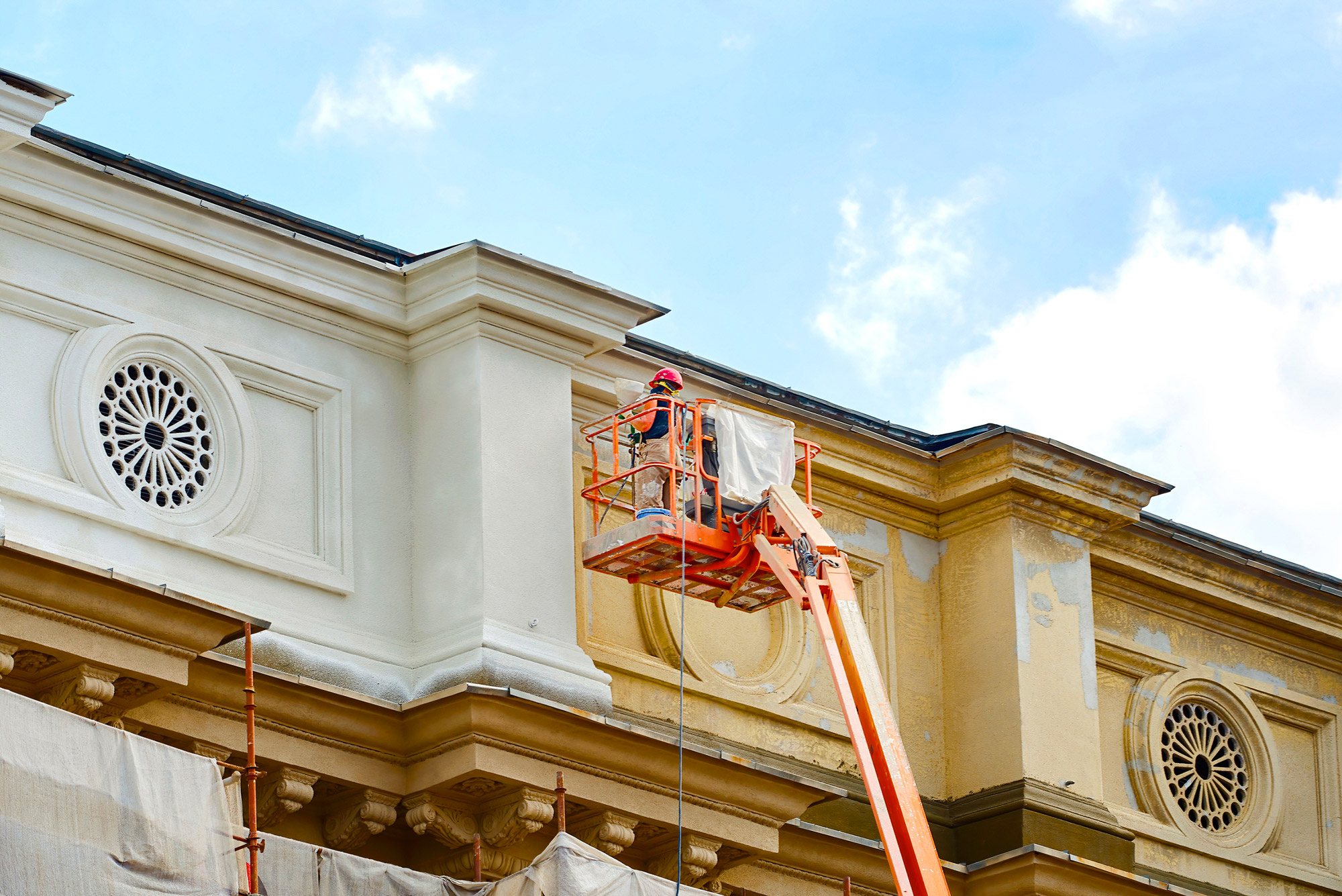 Painter restoring and repainting ornate commercial building facade using boom lift