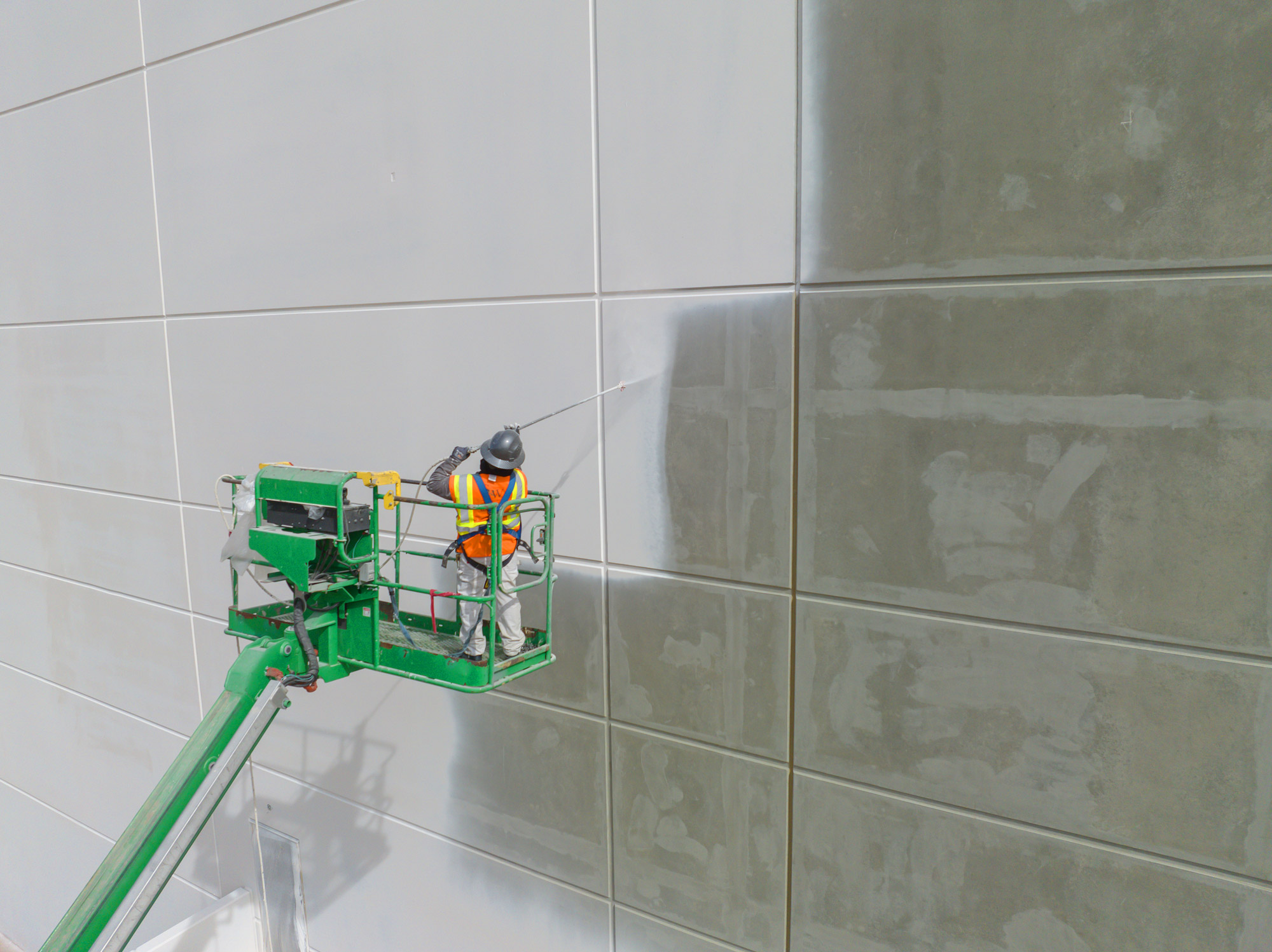 Commercial painter using a boom lift to apply white paint on a precast concrete wall during a commercial building repainting project