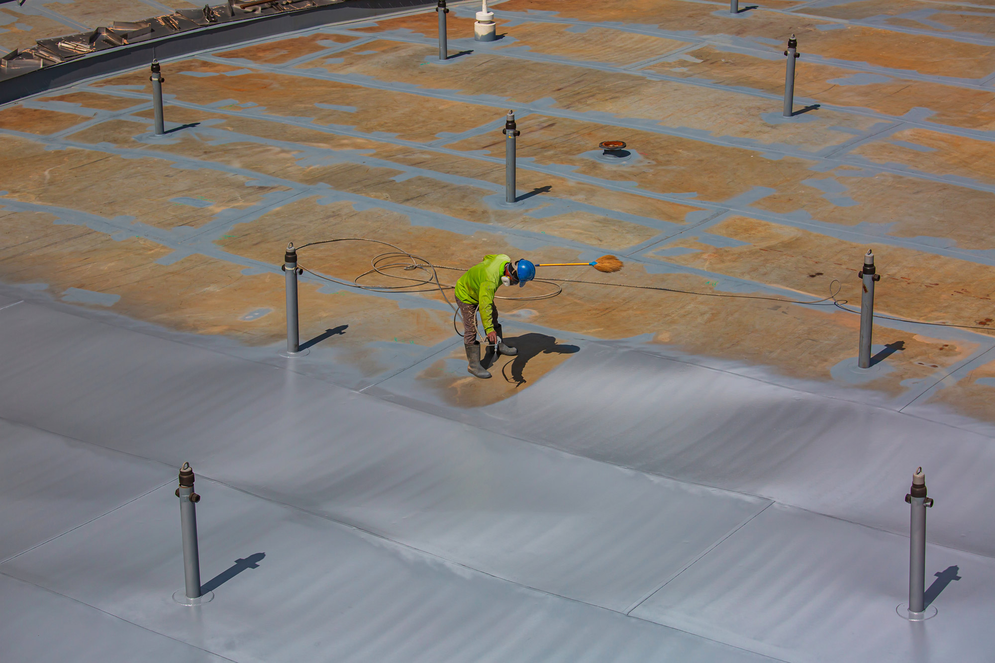 Technician applying protective coating to industrial roof surface with spray equipment
